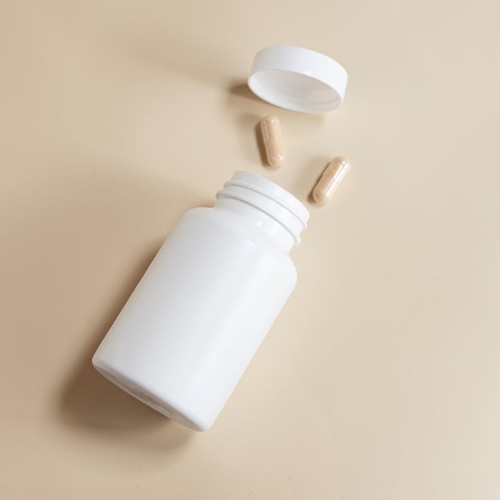 Minimalist image of a white medicine bottle with capsules on a soft beige background, perfect for health-related content.